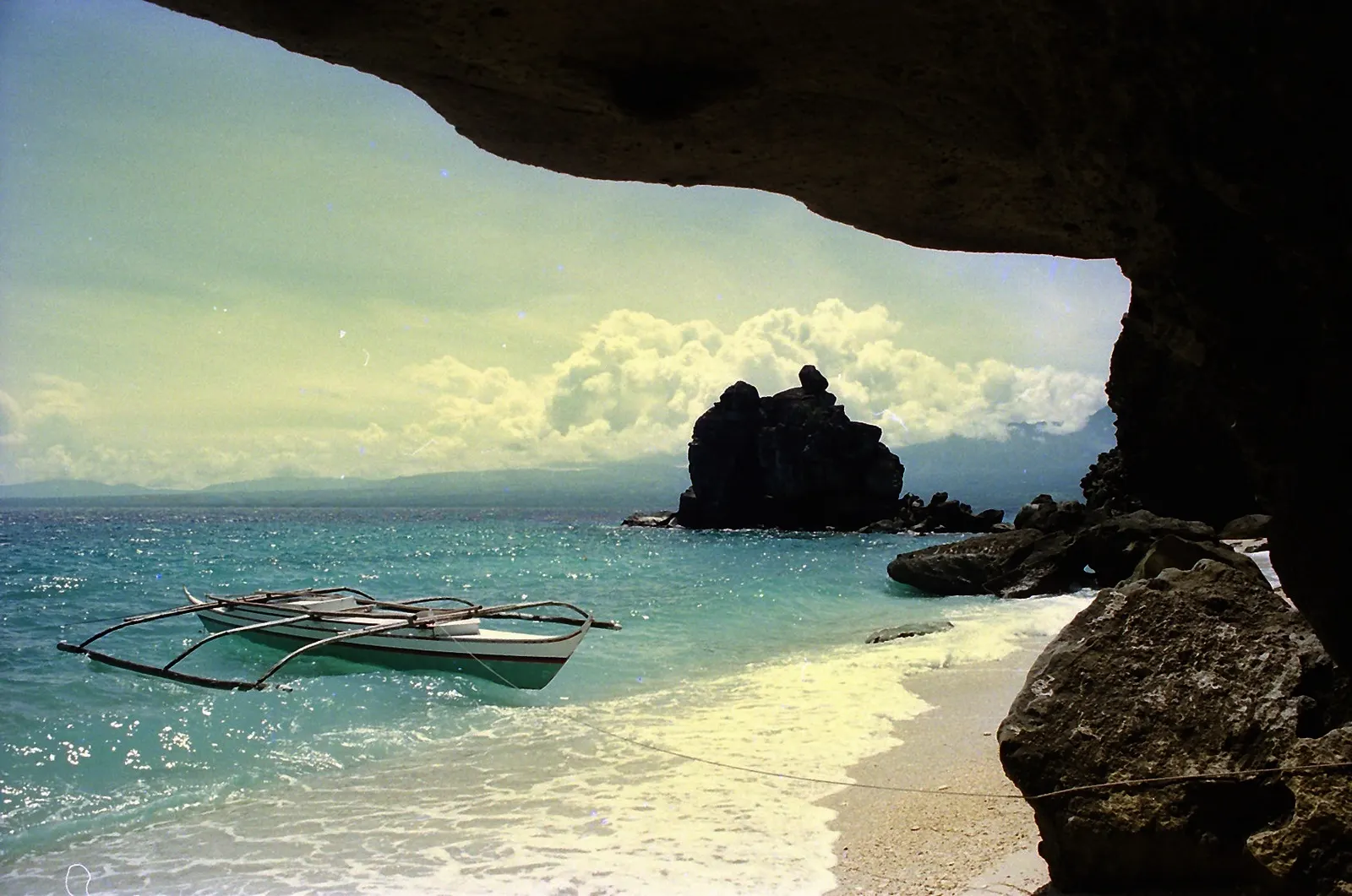 Outrigger boat moored off a white-sand beach framed by rocks on Apo Island, Negros Oriental