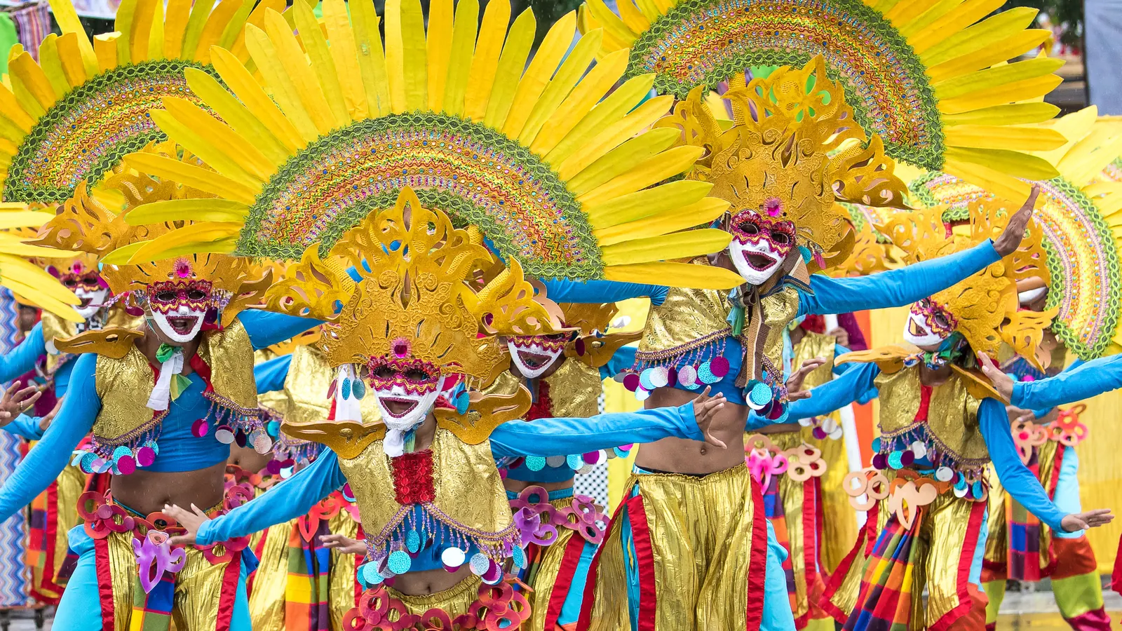 MassKara Festival dancers in Bacolod wearing brightly coloured smiling masks and gold feathered headdresses