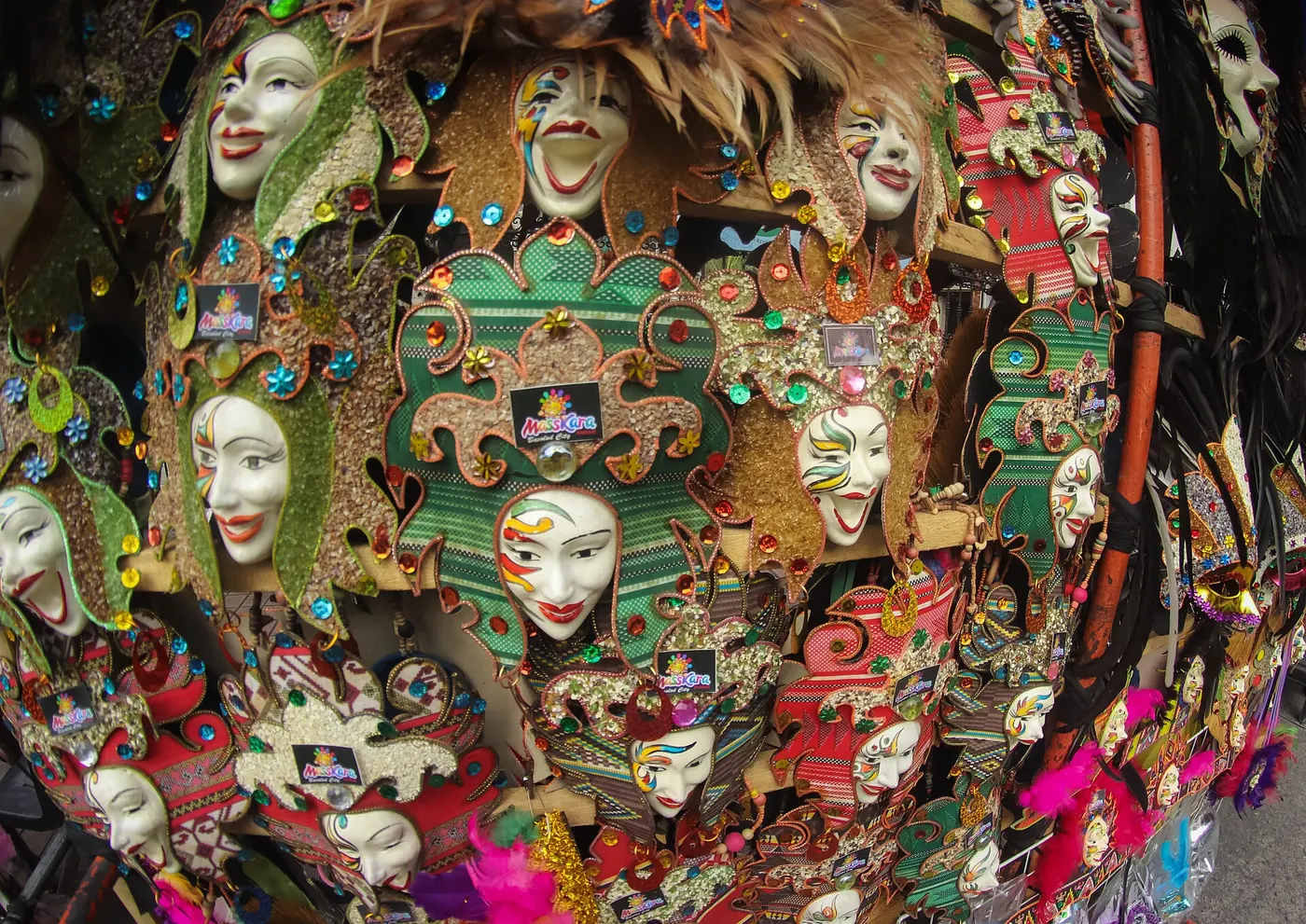 A street stall in Bacolod hung with handmade MassKara souvenir masks, each a painted smiling face framed in sequins, beads and woven fabric