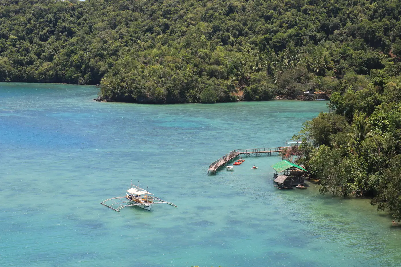 Pump boat floating in a turquoise cove ringed by jungle in Sipalay, Negros Occidental